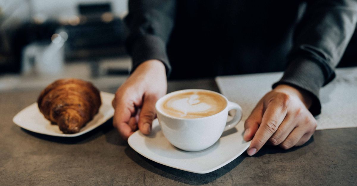 A barista places a latte and croissant on a counter, creating a warm cafe atmosphere.